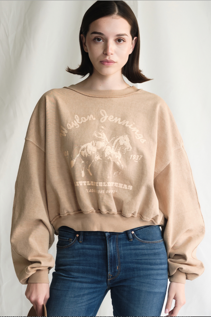 Person wearing a beige sweatshirt with graphic design and blue jeans on a plain background